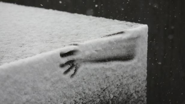Auf einer schneebedeckten Oberfläche ist ein Handabdruck zu sehen.