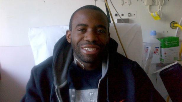 Ein lächelnder Mann sitzt in einem Krankenhausbett.