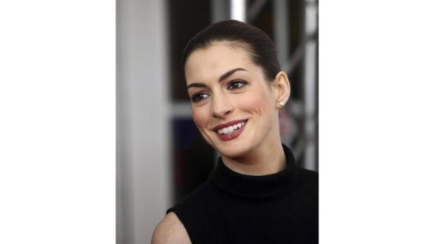 Ein Porträt von Anne Hathaway, die lächelt und ein schwarzes Oberteil trägt.