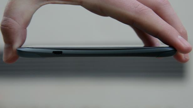 Eine Hand hält ein schwarzes Smartphone seitlich, wobei der USB-Anschluss sichtbar ist.