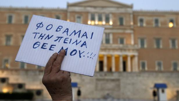 Eine Person hält ein Schild mit griechischem Text vor einem Gebäude.