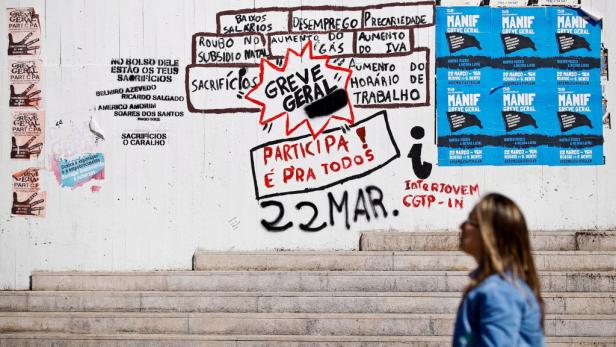 Eine Frau geht an einer Wand mit Graffiti und Protestplakaten vorbei.