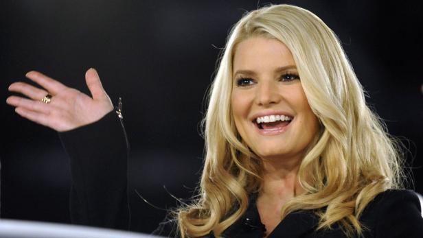 Jessica Simpson lächelt und winkt in einem schwarzen Blazer.