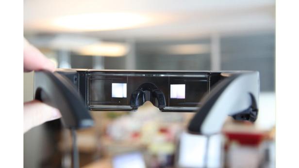 Eine Hand hält eine Augmented-Reality-Brille vor einem verschwommenen Hintergrund.