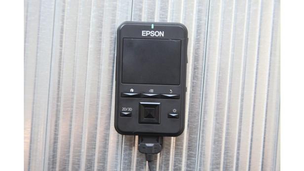 Eine schwarze Epson-Fernbedienung vor einem silbernen, geriffelten Hintergrund.