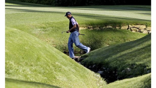 Ein Golfer überquert einen kleinen Bach auf einem Golfplatz.