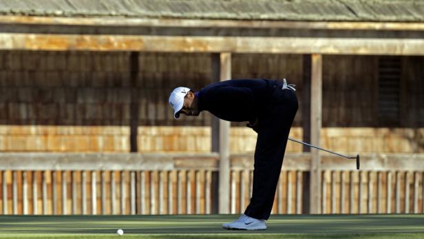 Ein Golfspieler beugt sich über den Golfball auf dem Grün.
