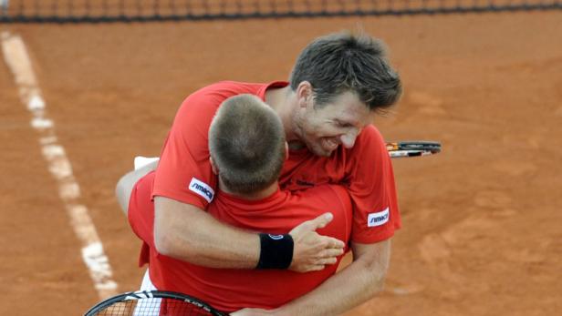 Zwei Tennisspieler umarmen sich auf einem Sandplatz.