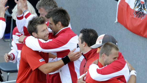 Österreichische Tennisspieler umarmen sich mit einer österreichischen Flagge im Hintergrund.