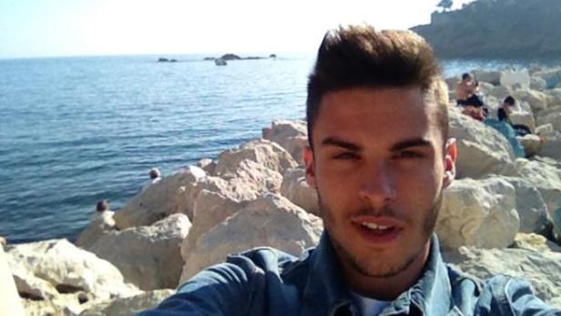 Ein junger Mann macht ein Selfie vor einer felsigen Küstenlandschaft.