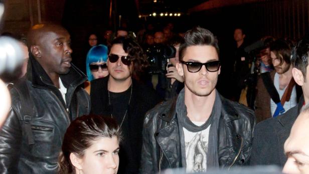 Mehrere Personen, darunter ein Mann mit blauen Haaren, stehen im Blitzlichtgewitter.