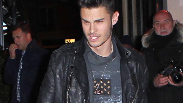 Ein Mann mit Lederjacke und Halskette blickt zur Seite.