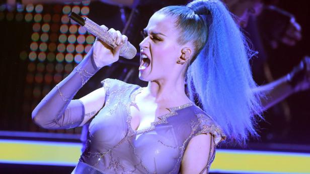 Katy Perry singt mit blau gefärbten Haaren in ein mit Strass besetztes Mikrofon.