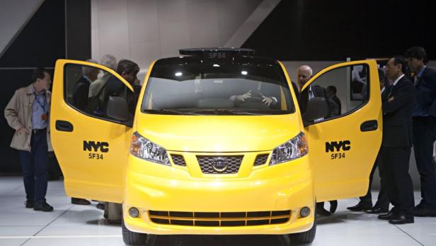 Ein gelbes Taxi mit offenen Türen und der Aufschrift „NYC SF34“ wird von Menschen umringt.