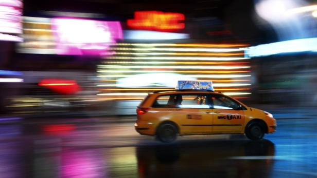 Ein gelbes Taxi fährt durch die nächtlichen Straßen von New York.
