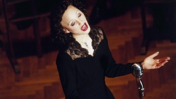 Eine Sängerin mit dunklem Haar und dunklem Kleid singt vor einem alten Mikrofon.