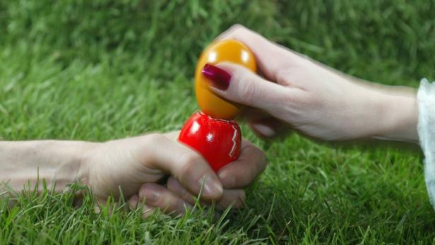 Zwei Personen schlagen Ostereier auf einer Wiese gegeneinander.