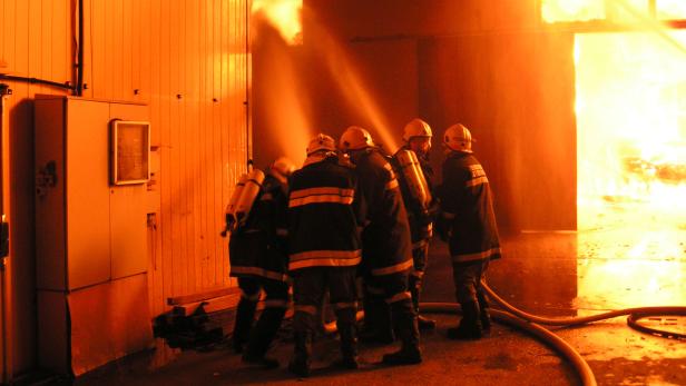 Eine Gruppe Feuerwehrleute steht vor einem brennenden Gebäude.