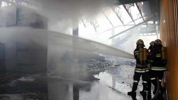 Feuerwehrleute bekämpfen einen Brand in einer Lagerhalle mit Wasserschläuchen.