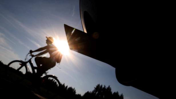 Ein Radfahrer fährt bei strahlendem Sonnenschein auf einer Straße entlang.