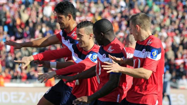 Eine Gruppe Fußballspieler in roten Trikots feiert ein Tor vor einer Zuschauermenge.