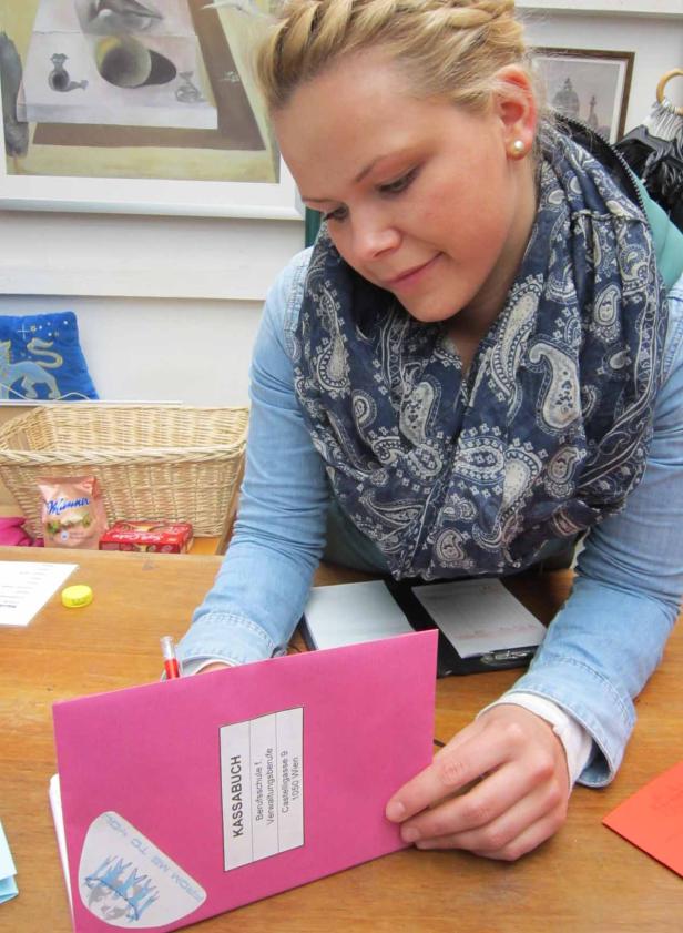 Eine junge Frau mit Zopf schreibt in ein Kassenbuch der Berufsschule für Verwaltungsberufe.