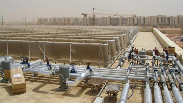 Auf einem Dach befinden sich Solarkollektoren und Rohrleitungen vor einer Wüstenlandschaft.