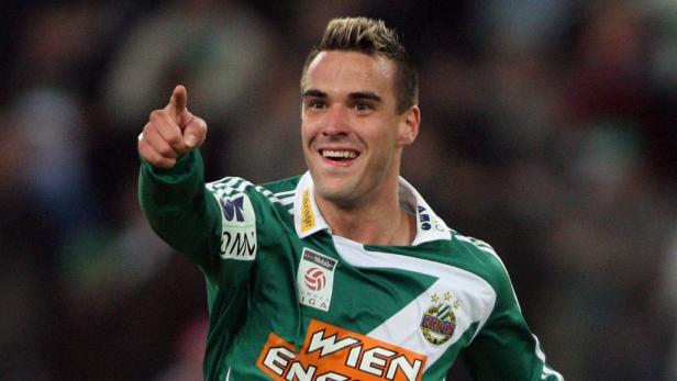 Ein lächelnder Fußballspieler von Rapid Wien zeigt mit dem Finger nach oben.