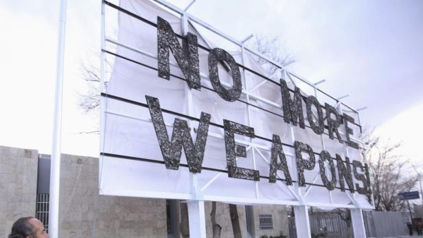 Eine große Tafel zeigt die Aufschrift „No More Weapons!“.