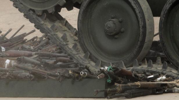 Ein Panzer fährt über einen Haufen von Gewehren.