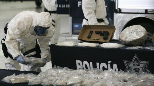 Polizisten in Schutzanzügen beschlagnahmen Drogen und eine Waffe.