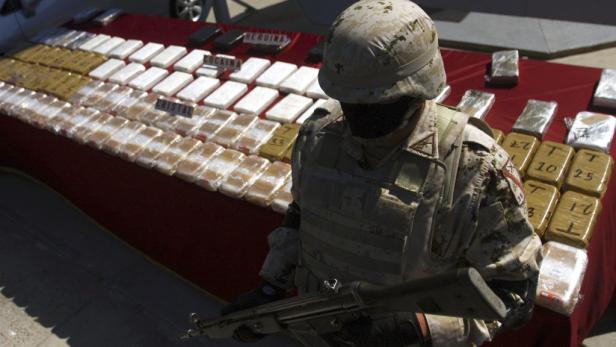 Ein Soldat steht mit einem Gewehr vor einem Tisch mit beschlagnahmten Drogen wie Kokain und Heroin.