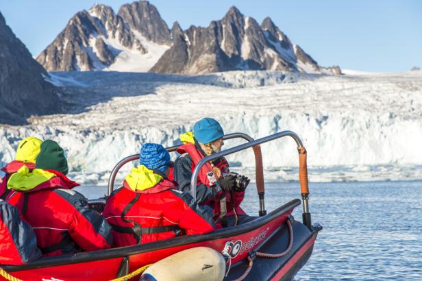 Eine Gruppe von Menschen fährt mit einem roten Schlauchboot an einem Gletscher vorbei.
