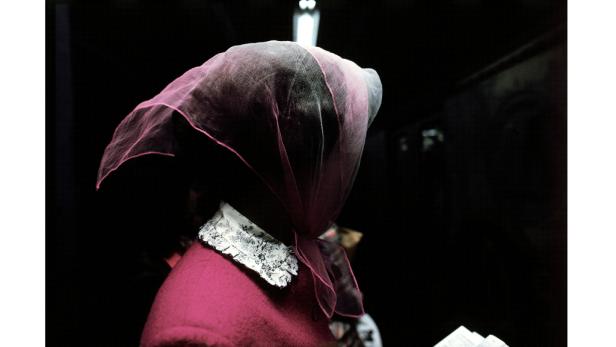 Eine Frau mit einem rosa Schleier und einem roten Oberteil mit Spitzenkragen.