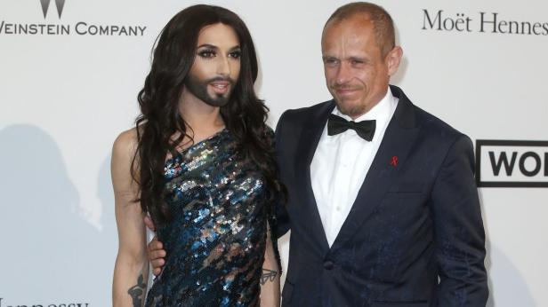 Conchita Wurst und ein Mann im Anzug posieren für ein Foto.