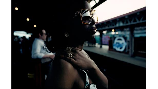 Eine Frau mit Sonnenbrille wartet an einem Bahnsteig.