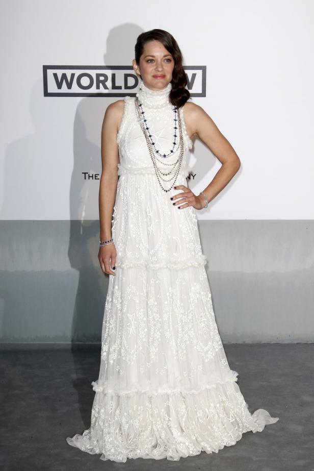 Marion Cotillard trägt ein langes, weißes Kleid mit Spitze und mehrere Halsketten.
