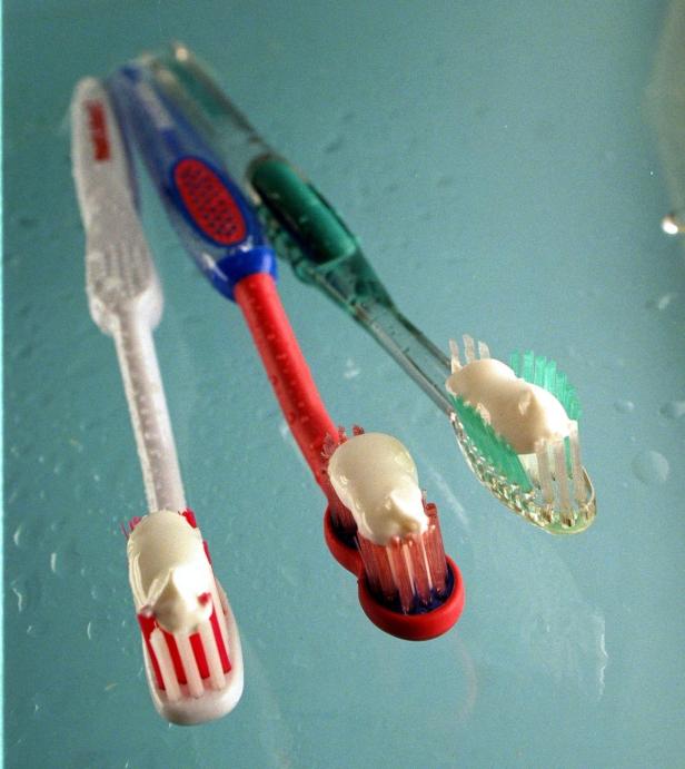 Drei Zahnbürsten mit Zahnpasta auf einer hellblauen Oberfläche.