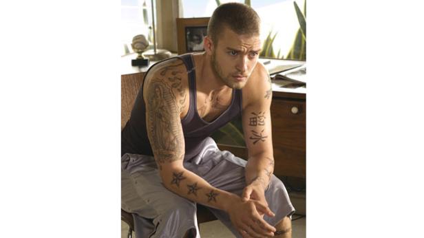 Justin Timberlake sitzt mit Tattoos auf den Armen auf einem Stuhl.