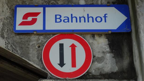 Ein blaues Schild mit der Aufschrift „Bahnhof“ und ein Verkehrsschild mit Pfeilen in beide Richtungen.