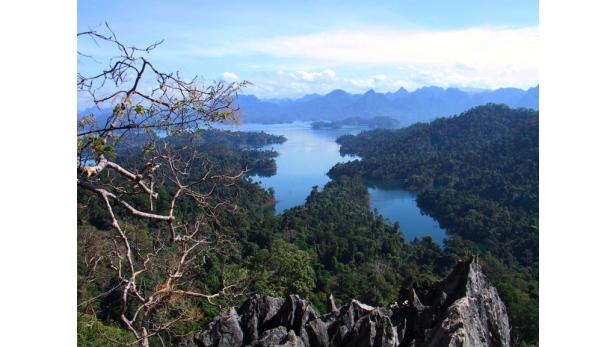 Blick von einem Felsen auf einen See mit bewaldeten Inseln und Bergen im Hintergrund.