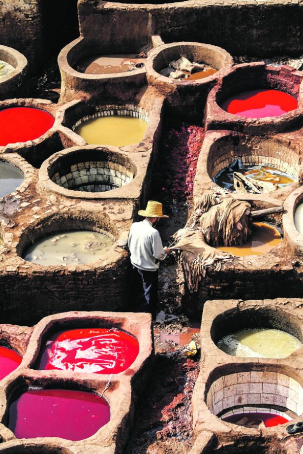 Ein Mann arbeitet in einer traditionellen Gerberei mit farbigen Becken in Fès, Marokko.