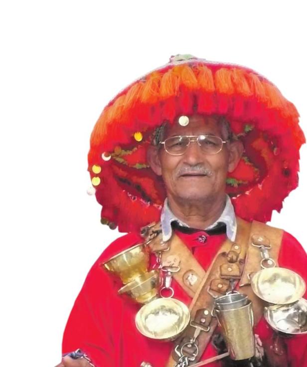 Ein Mann mit Brille und einem großen, roten Hut, geschmückt mit goldenen Objekten.