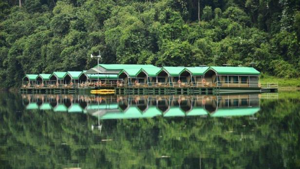 Eine Reihe von schwimmenden Bungalows mit grünen Dächern auf einem ruhigen See.