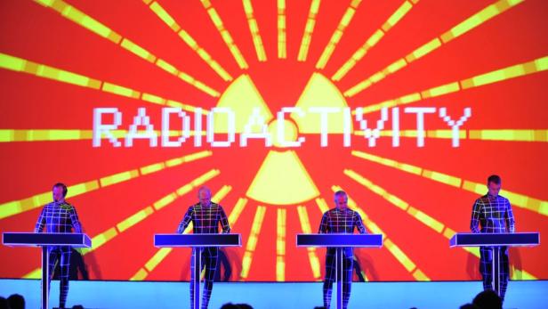 Die Band Kraftwerk tritt vor einer Projektion des Schriftzugs „Radioactivity“ auf.