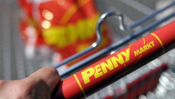 Eine Hand schiebt einen Einkaufswagen von Penny Markt.
