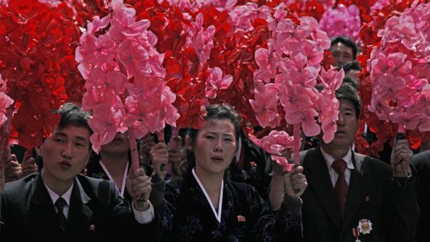 Menschen in Nordkorea halten rote und pinke Papierblumen bei einer Parade.
