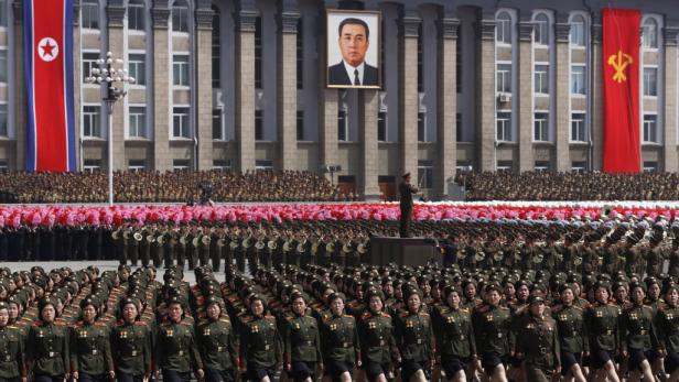 Eine Militärparade in Nordkorea mit Soldaten und Musikkapellen vor einem Porträt von Kim Il-sung.
