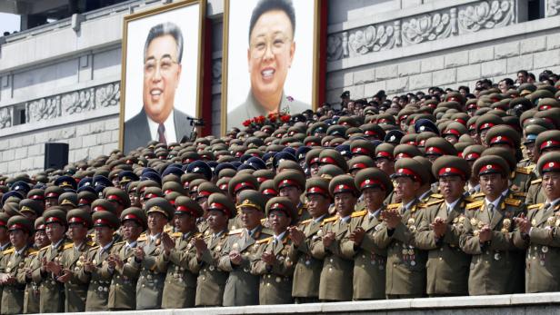 Eine Menschenmenge in Uniform klatscht vor Porträts nordkoreanischer Führer.
