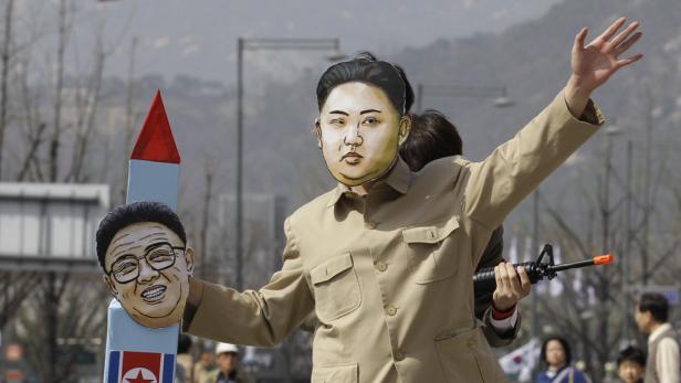 Eine Person mit einer Kim-Jong-Un-Maske hält eine Spielzeugwaffe und eine Raketenattrappe.
